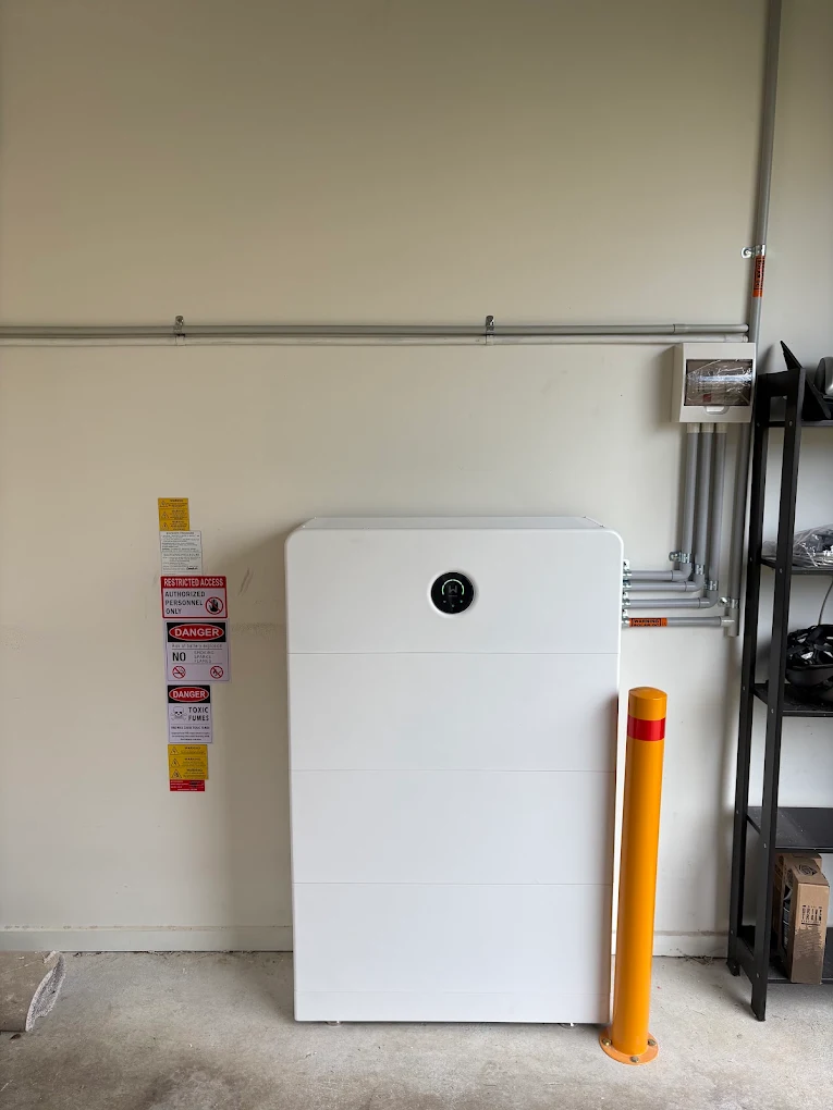 Home battery system installed in a garage with neat conduit and safety signage
